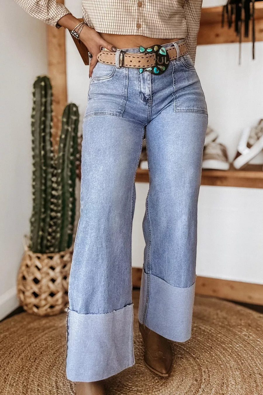 Person wearing blue jeans and brown boots indoors with a cactus plant in the background
