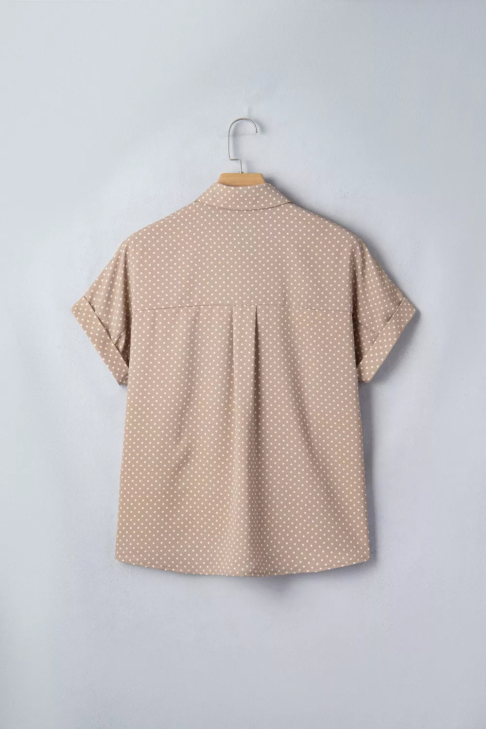 Beige polka dot shirt on a hanger against a light gray background