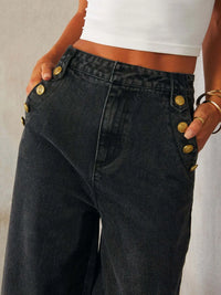 Black jeans with gold buttons worn by a person against a neutral background