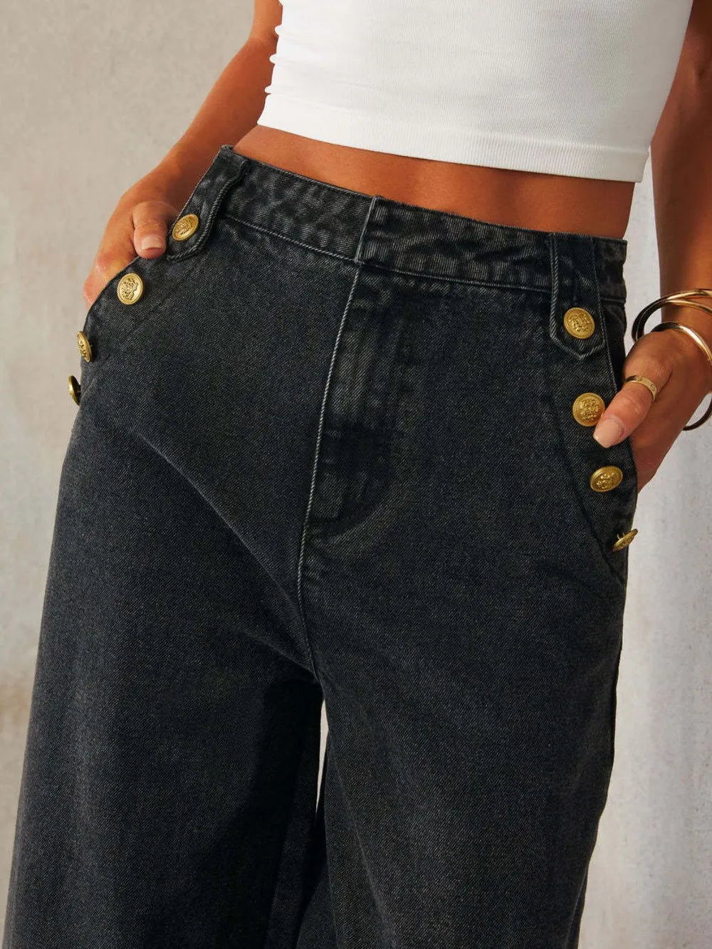Black jeans with gold buttons worn by a person against a neutral background