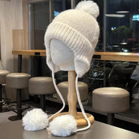 White knitted hat with pom-poms on a mannequin head in a cafe setting