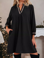 Woman wearing a black dress with decorative trim in a festive indoor setting.