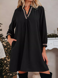 Woman wearing a black dress with decorative trim in a festive indoor setting.