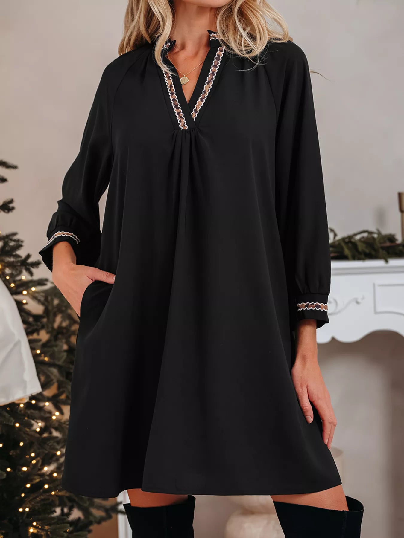 Woman wearing a black dress with decorative trim in a festive indoor setting.