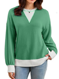Green ribbed sweater with white trim worn by a person on a white background