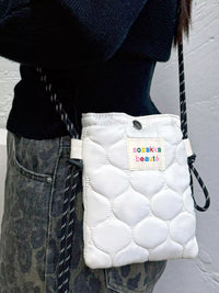 White quilted pouch with 'sozakia beauty' label held by a person wearing a black sweater and denim jeans.