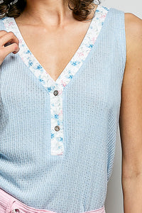 Light blue sleeveless top with floral trim and buttons on a neutral background