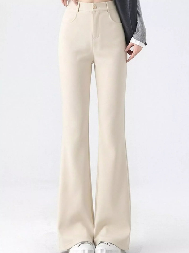 A person wearing high-waisted, straight-leg or bootcut pants in a light cream/beige color, styled with a gray cardigan and white sneakers against a plain white studio background.