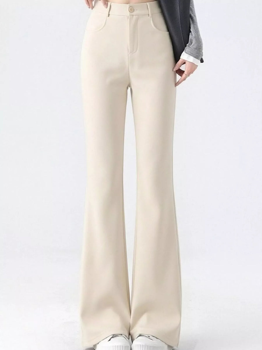 A person wearing high-waisted, straight-leg or bootcut pants in a light cream/beige color, styled with a gray cardigan and white sneakers against a plain white studio background.