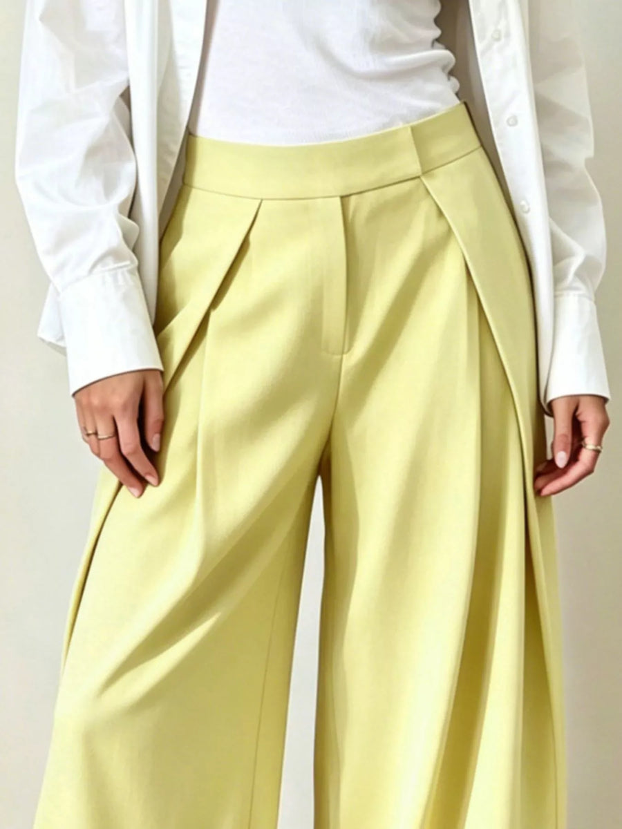 Person wearing light yellow pleated pants with a white shirt and jacket.