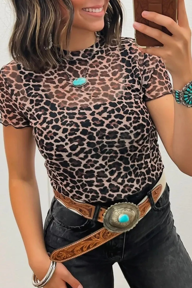 Person wearing a leopard print top and black pants with a belt, holding a phone.