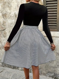 Person wearing a black long-sleeve top and a gray and white striped skirt against a stone wall.