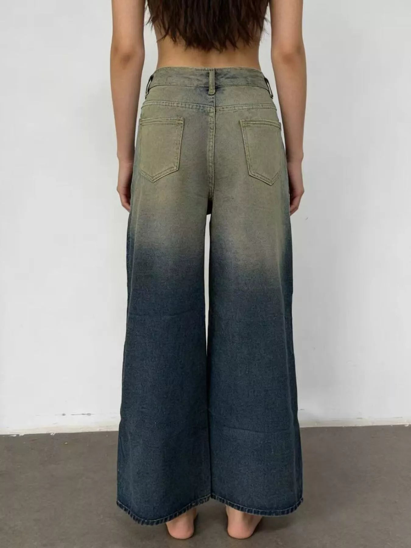 Person wearing a pair of wide-leg jeans with a gradient effect against a plain background