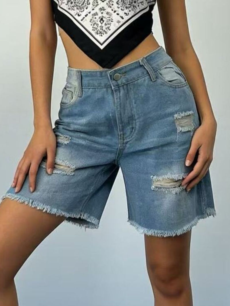 Person wearing distressed denim shorts on a plain background