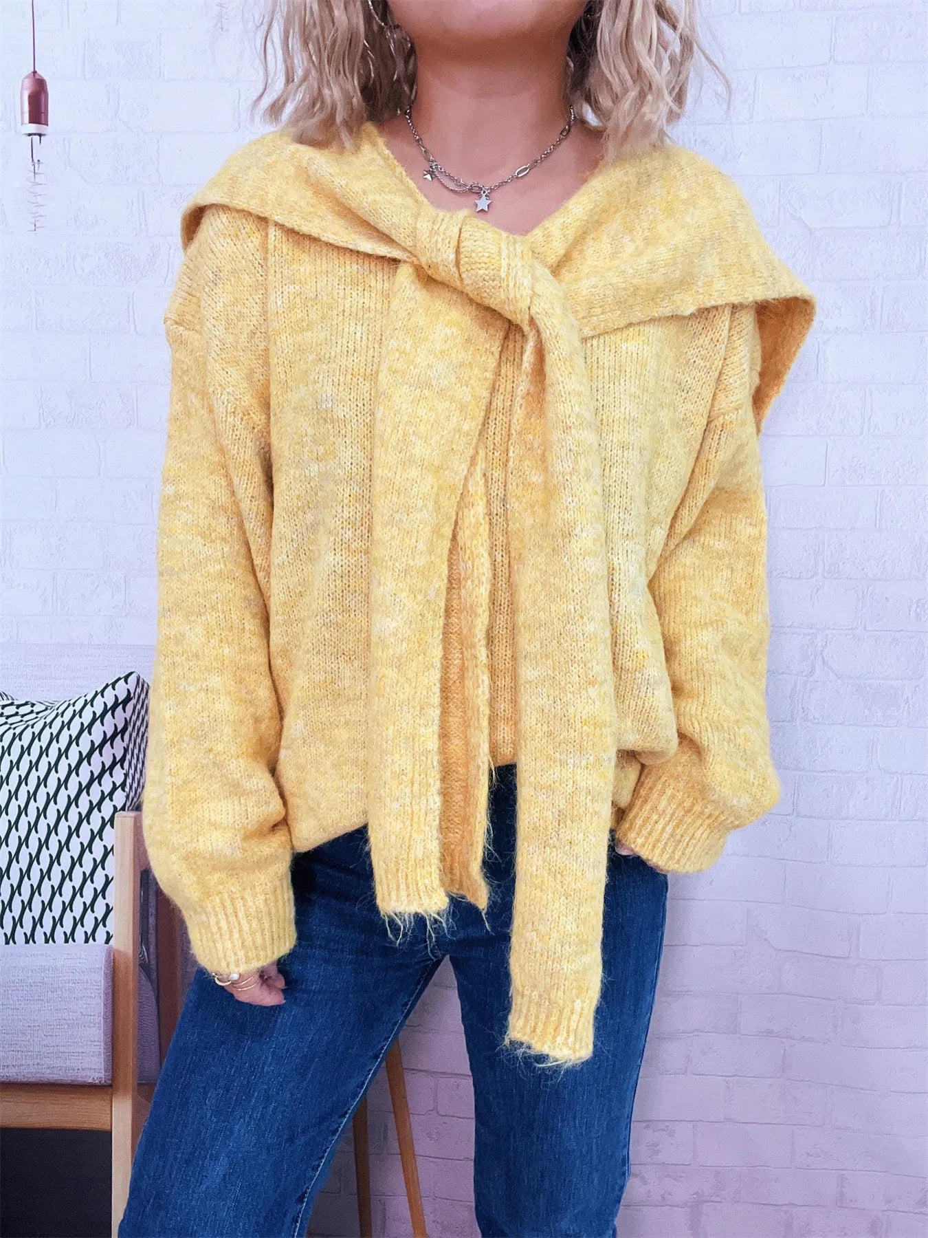 Person wearing a yellow knitted cardigan with a white brick wall background