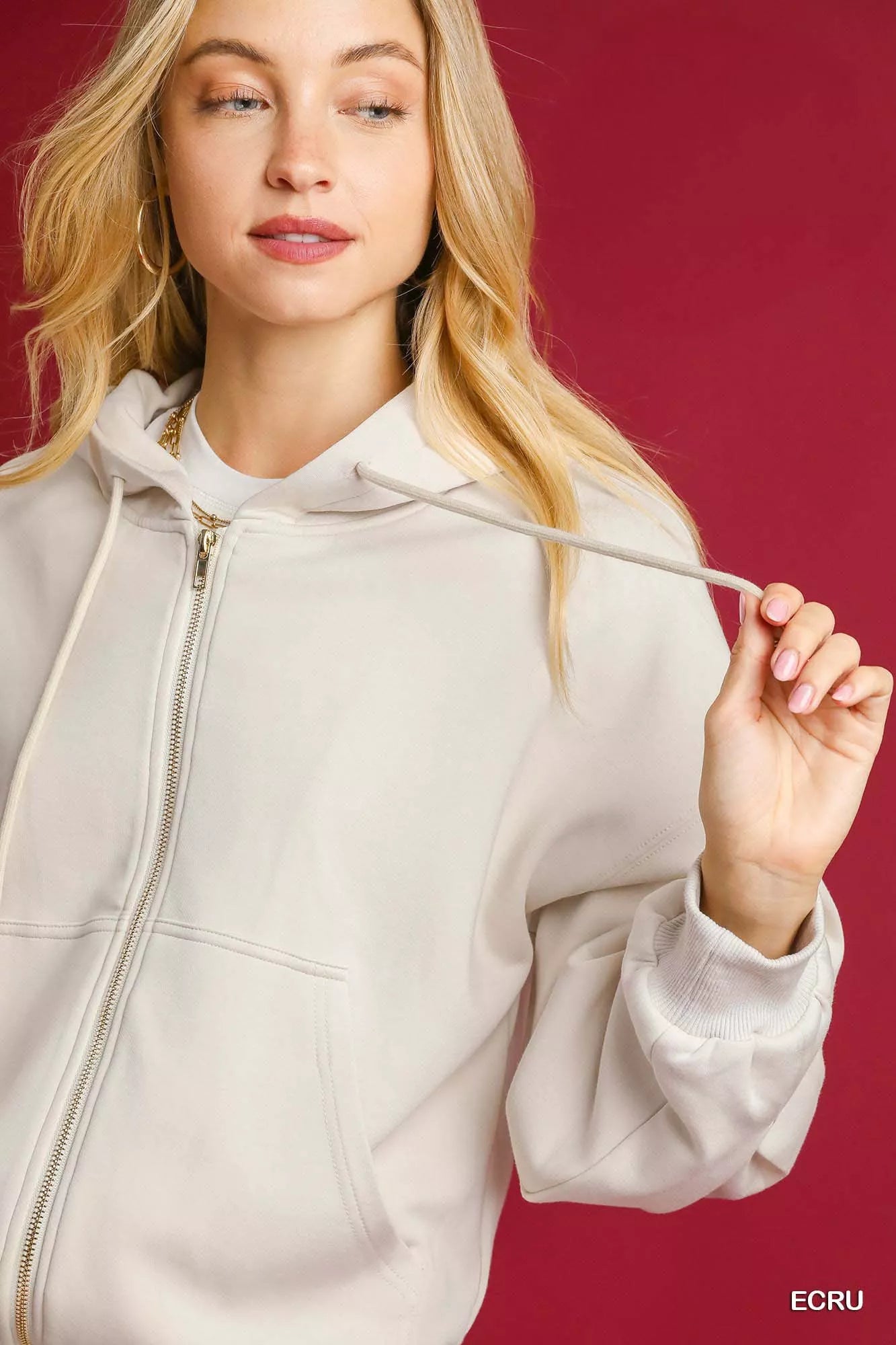 Woman wearing a beige hoodie against a red background