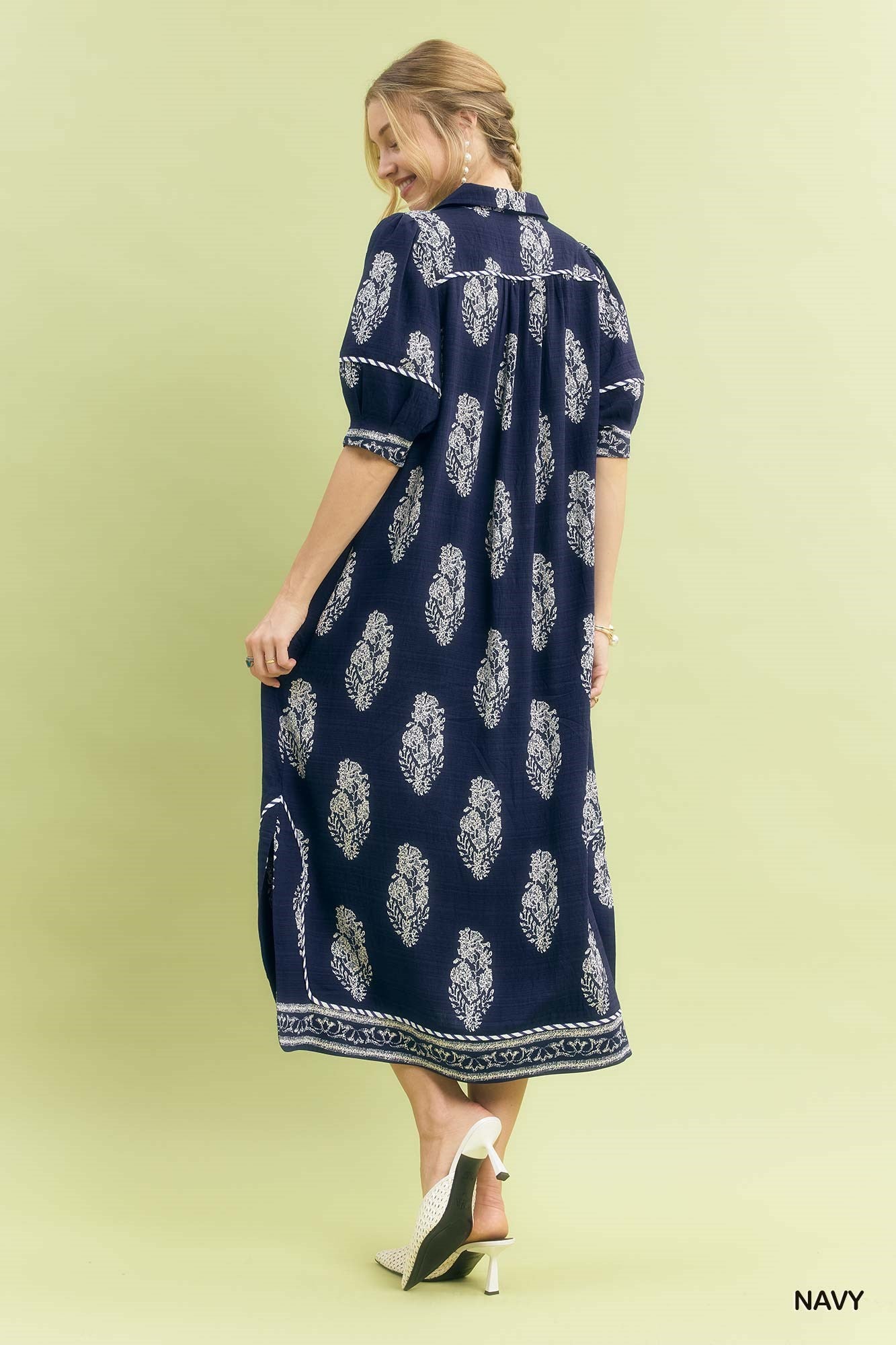 Woman wearing a navy dress with white floral pattern on a light green background