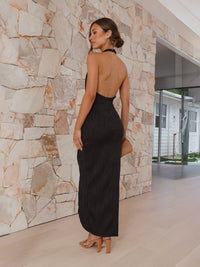 Woman in a black dress standing against a stone wall.