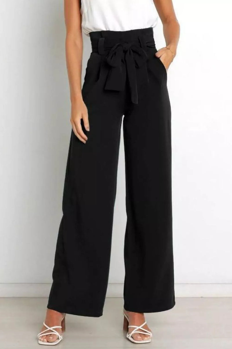 Person wearing black wide-leg pants with a white top against a plain background