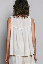 Person wearing a sleeveless white top with a textured pattern on a plain background