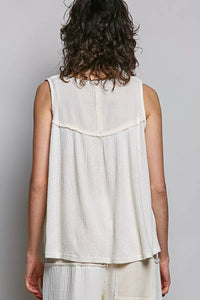 Person wearing a sleeveless white top with a textured pattern on a plain background