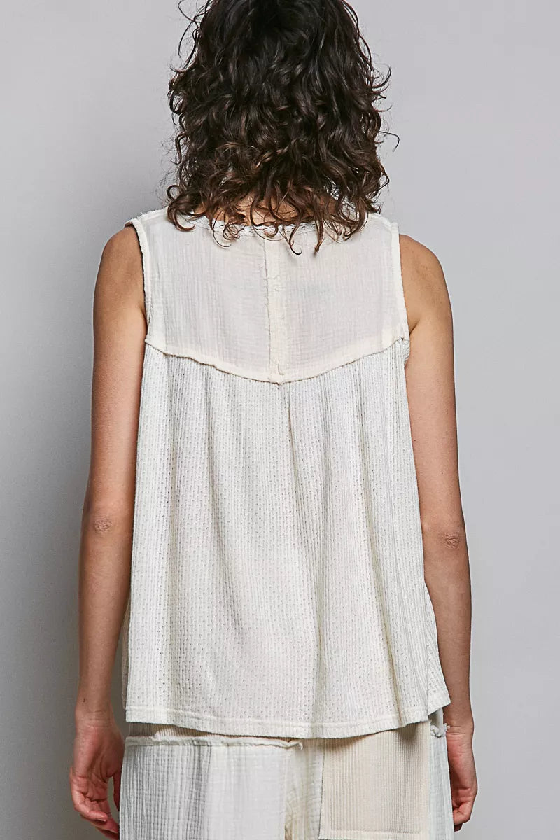Person wearing a sleeveless white top with a textured pattern on a plain background