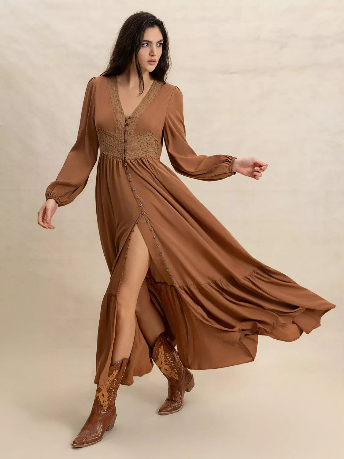 Woman wearing a long brown dress with a slit and matching boots on a beige background