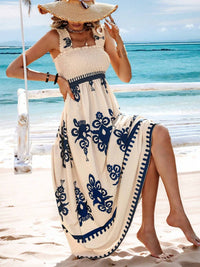 Woman in a beige and blue dress with a straw hat sitting on a beach swing by the ocean.