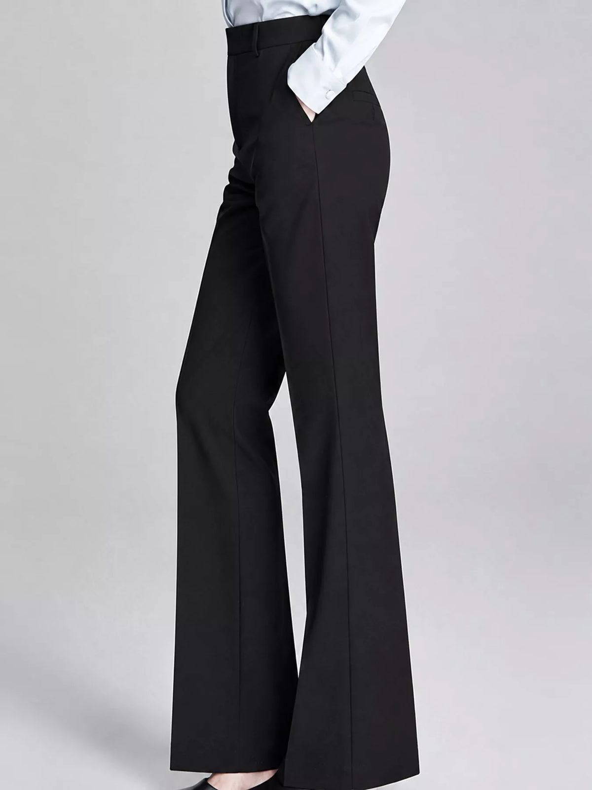 Black wide-leg trousers shown on a model from the waist down, paired with a white shirt and black shoes, against a light gray studio background.