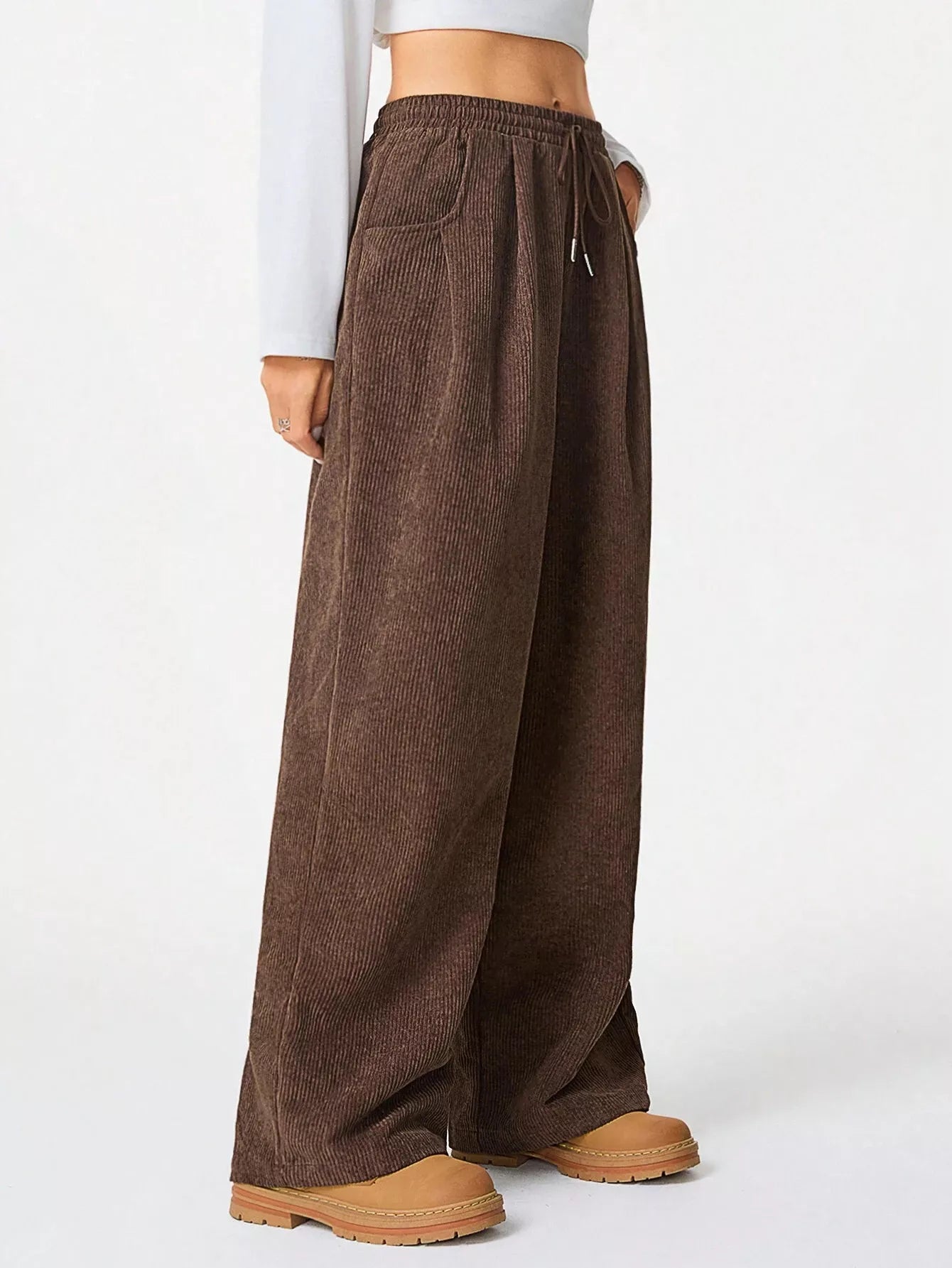 Brown wide-leg pants worn with a white top and brown shoes on a white background