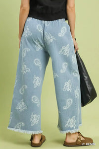 Light blue denim pants with white patterns worn by a person on a green background