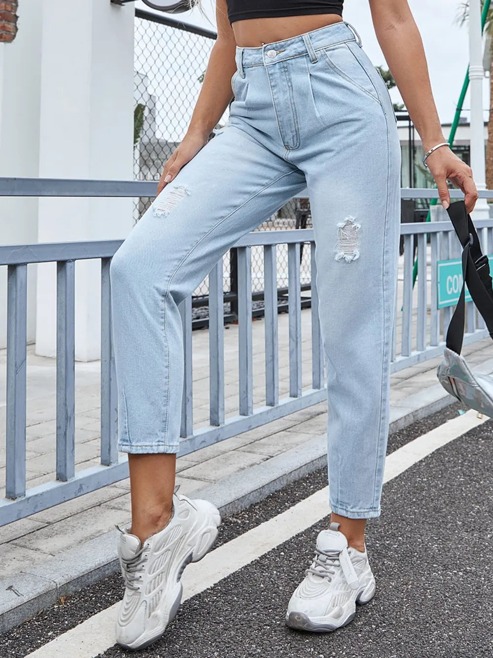 Person wearing light blue jeans and white sneakers on a street.