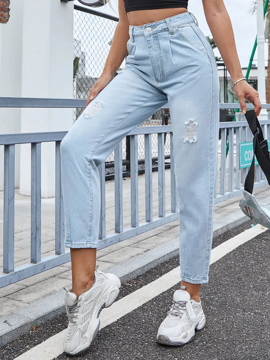 Person wearing light blue jeans and white sneakers on a street.