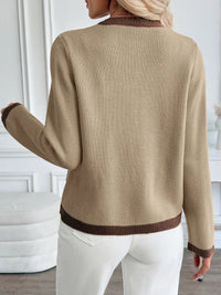 Person wearing a beige sweater with brown trim in an indoor setting