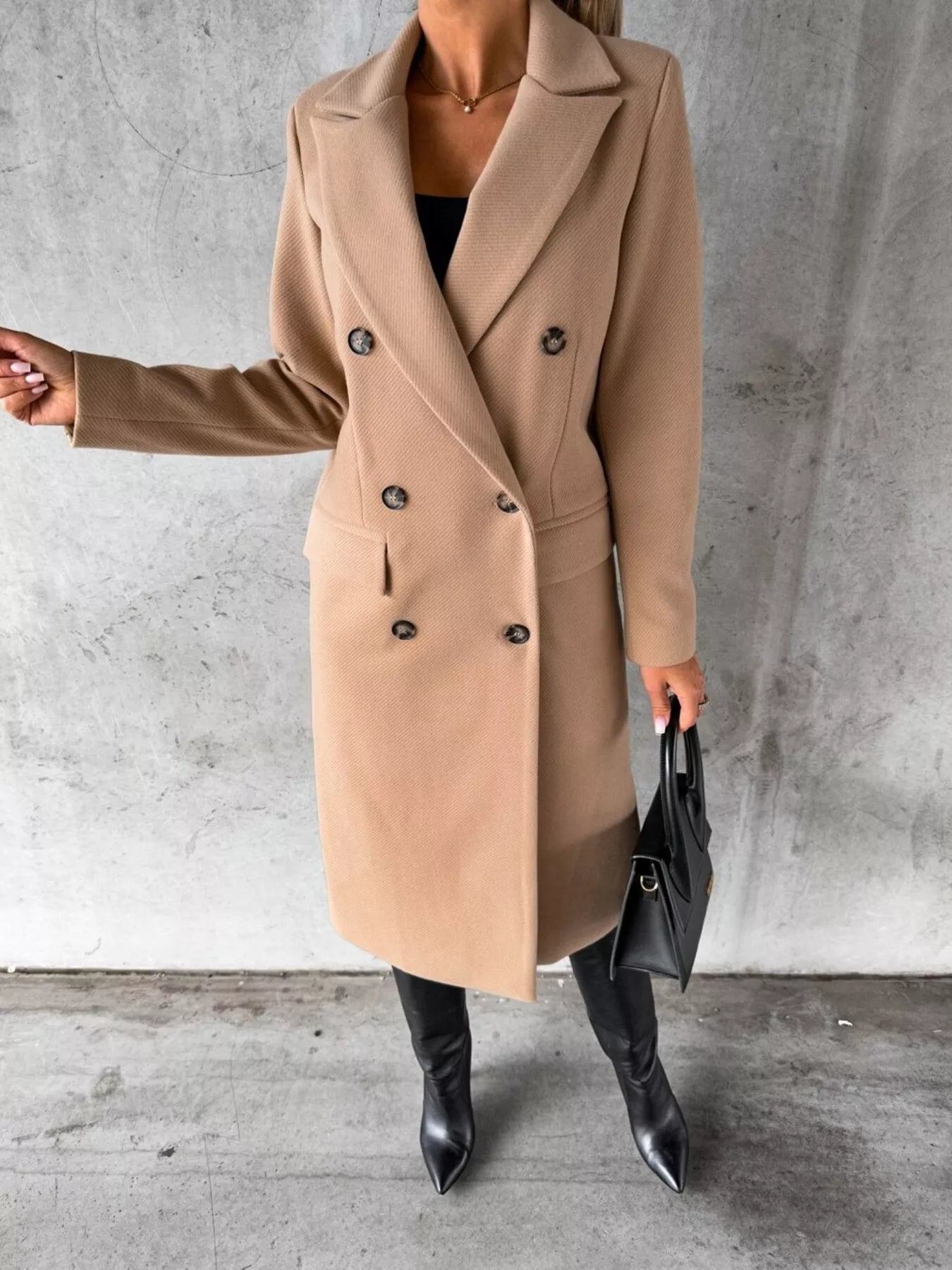 Person wearing a beige coat with black buttons against a gray concrete wall.