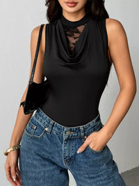 Person wearing a black sleeveless top and blue jeans against a gray background