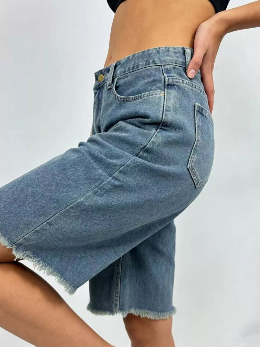 Blue denim shorts worn by a person on a plain background