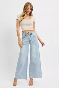 Woman wearing a beige crop top and light blue wide-leg jeans on a white background