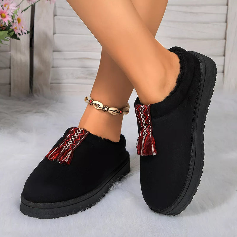 Black slippers with red tassels worn by a person on a light background