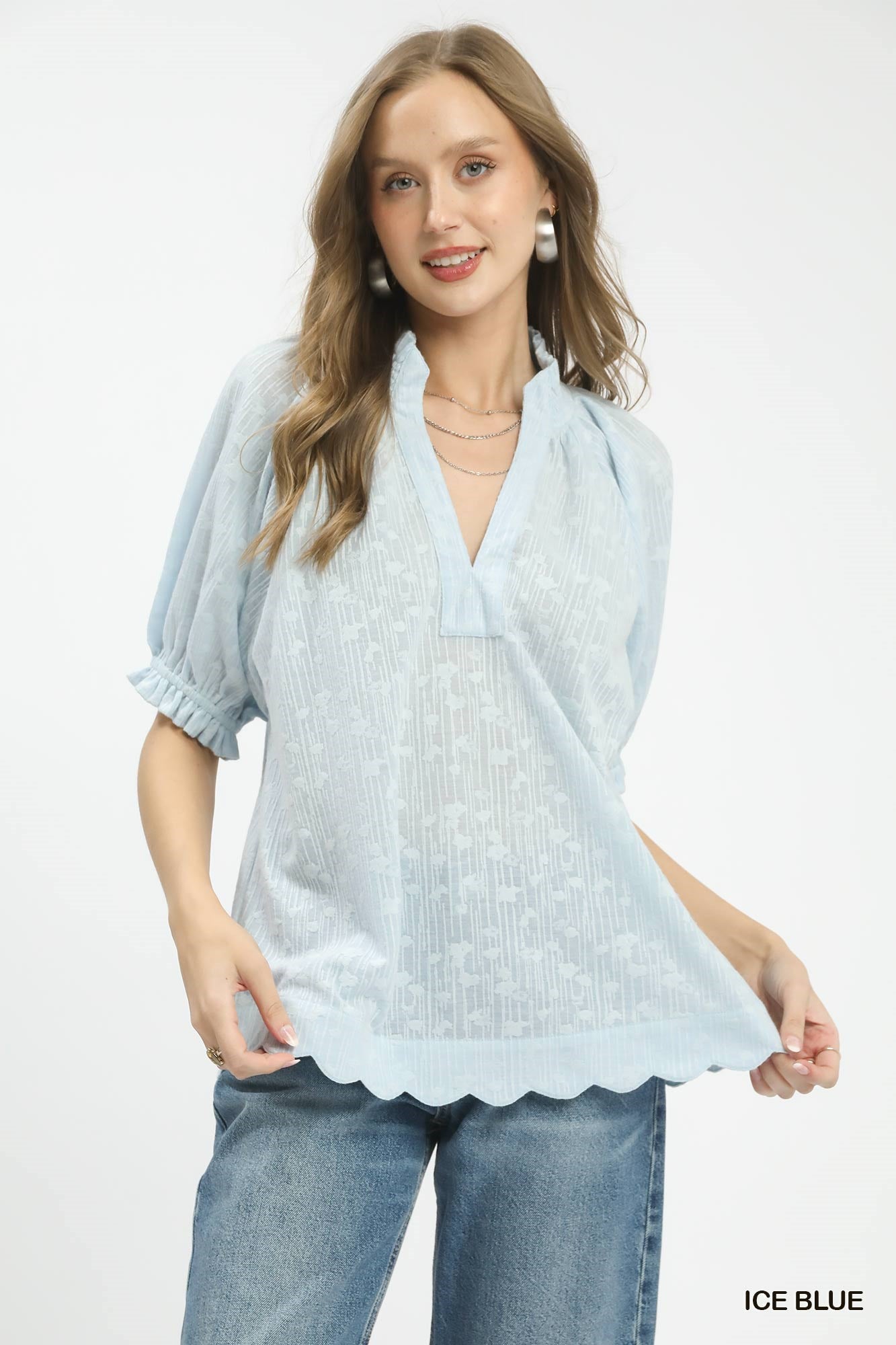 Woman wearing a light blue poncho with scalloped edges on a white background