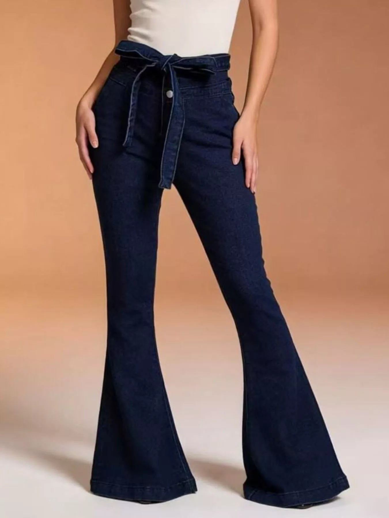 Navy blue flared jeans worn by a person on a beige background