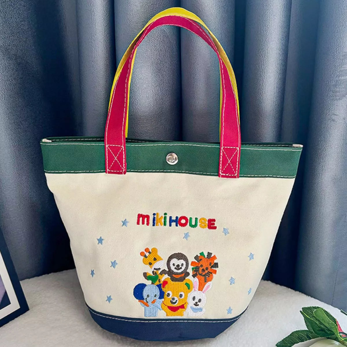 Tote bag with colorful handles and cartoon characters on a blue curtain background