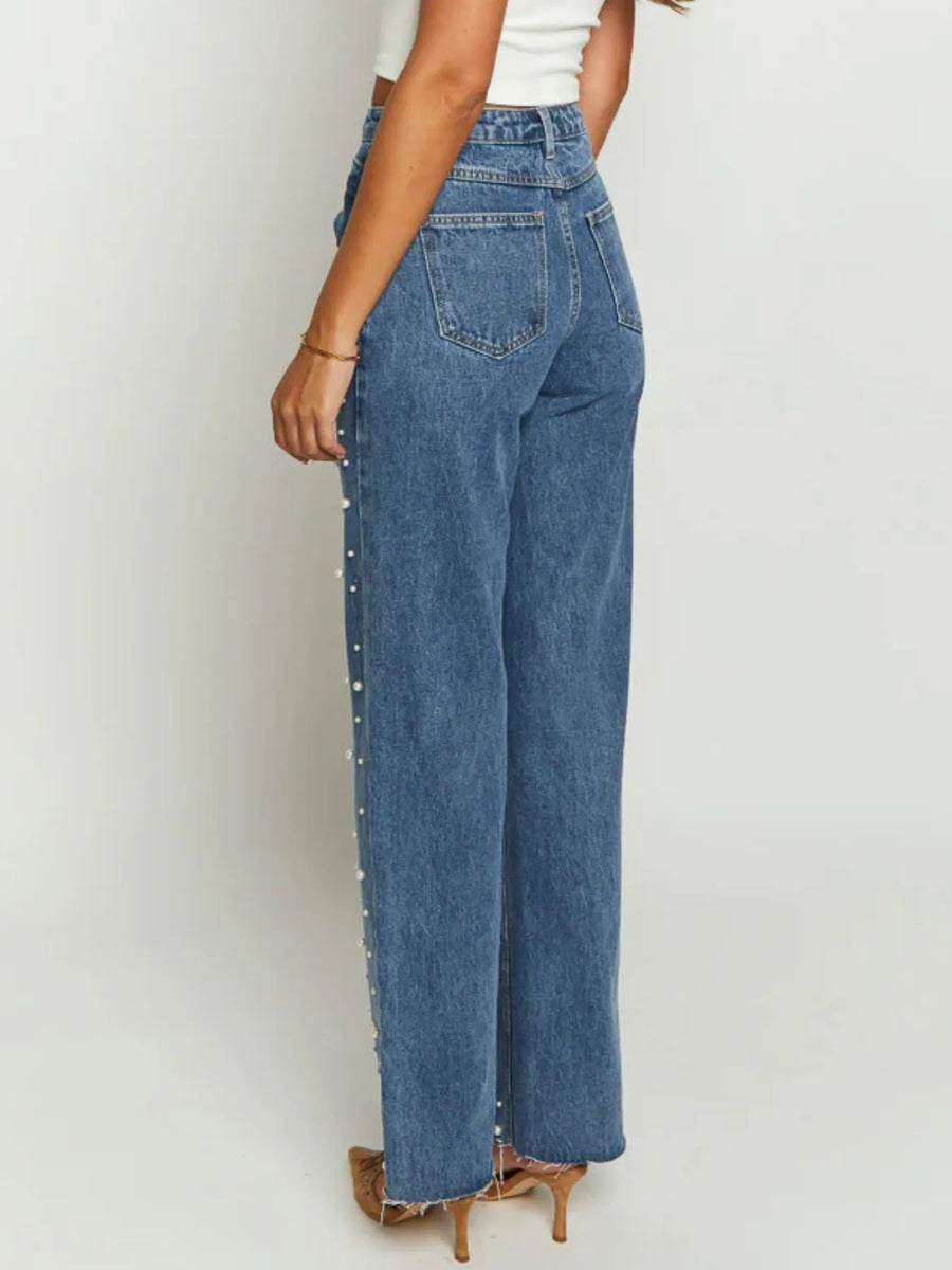 Person wearing blue jeans with decorative studs on a plain background