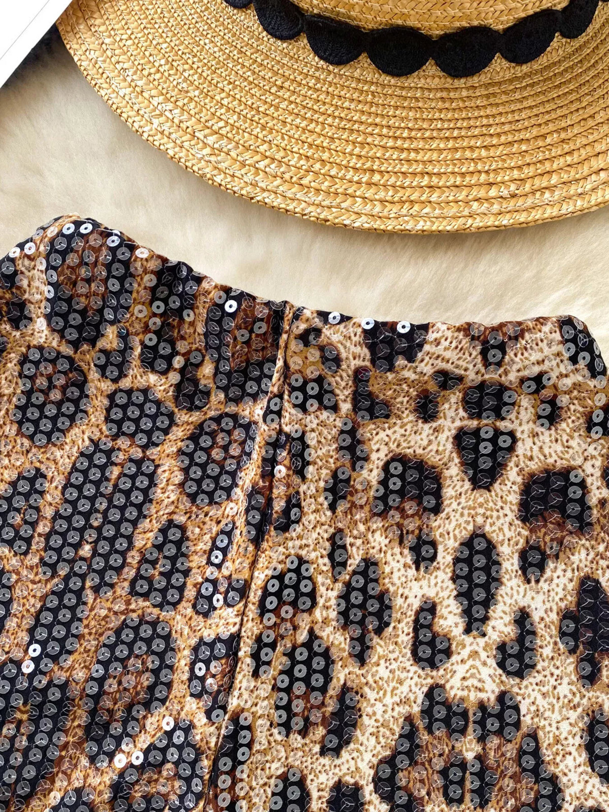 Leopard print clutch with sequins and a straw hat with black trim on a light background