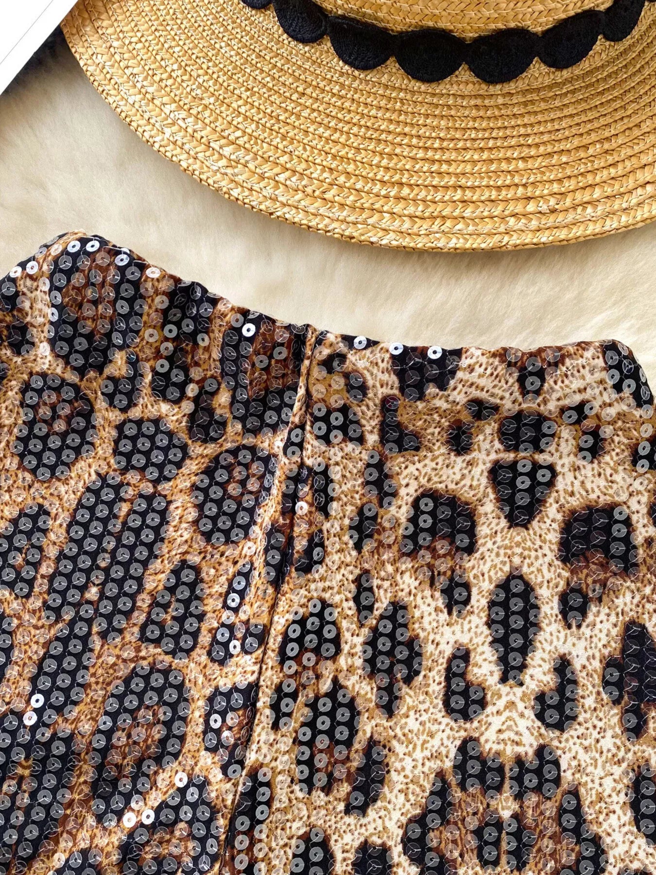 Leopard print clutch with sequins and a straw hat with black trim on a light background