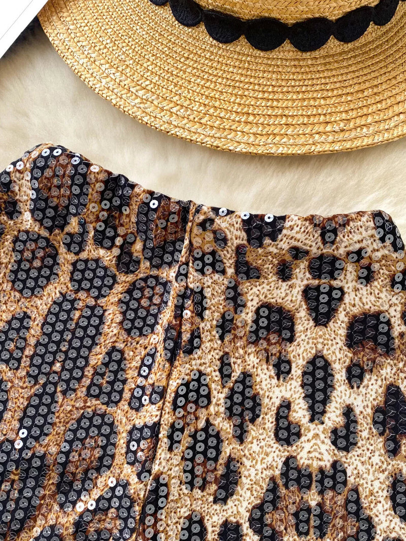 Leopard print clutch with sequins and a straw hat with black trim on a light background