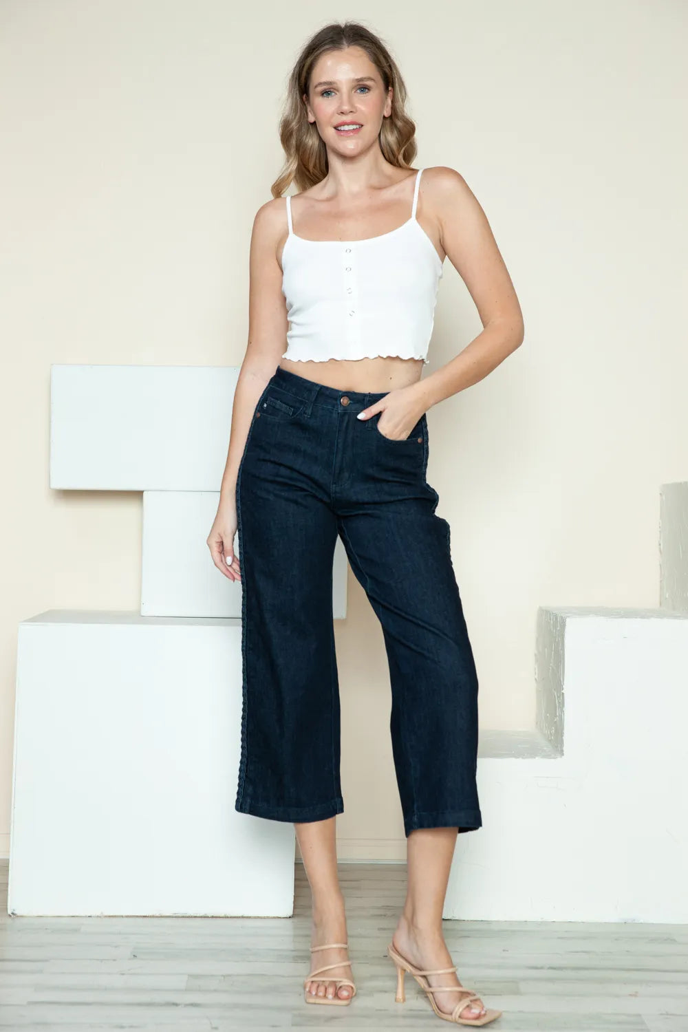 Woman wearing a white top and dark blue jeans against a light background