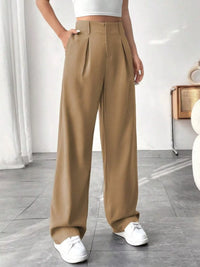 Person wearing beige wide-leg pants and white sneakers in a minimal indoor setting.