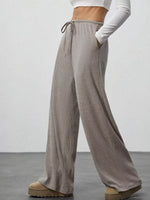 Person wearing gray wide-leg pants with a white top on a plain background