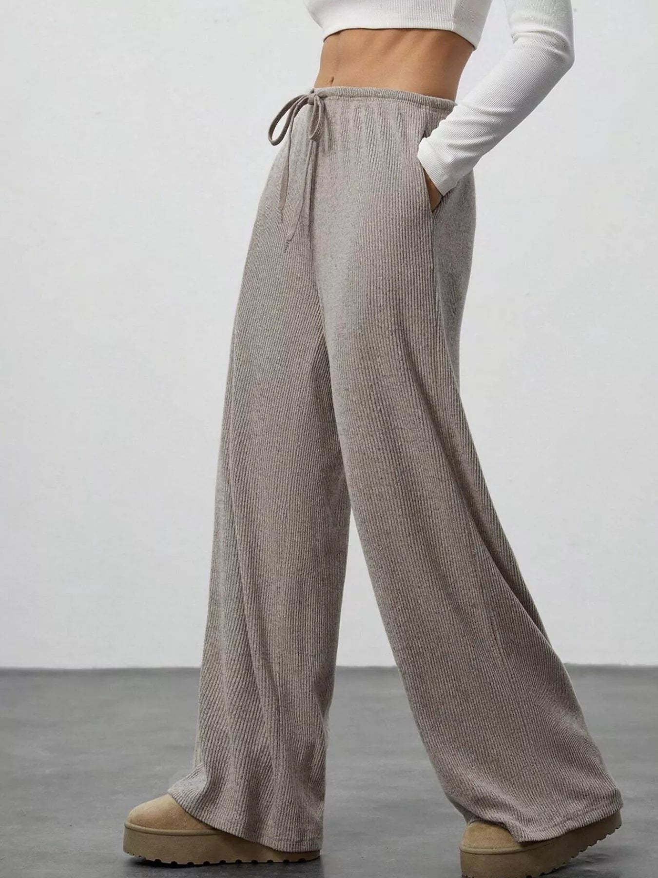 Person wearing gray wide-leg pants with a white top on a plain background